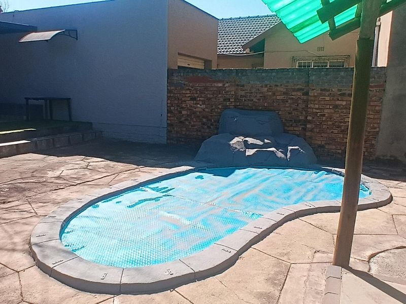 Outdoor pool area featuring a paved patio, brick boundary wall, and a covered swimming pool.