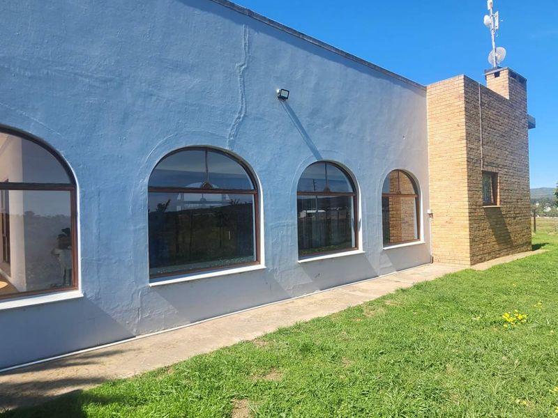 Rear view of the farm property featuring arched windows, a brick chimney, and a concrete walkway set against a grassy lawn.