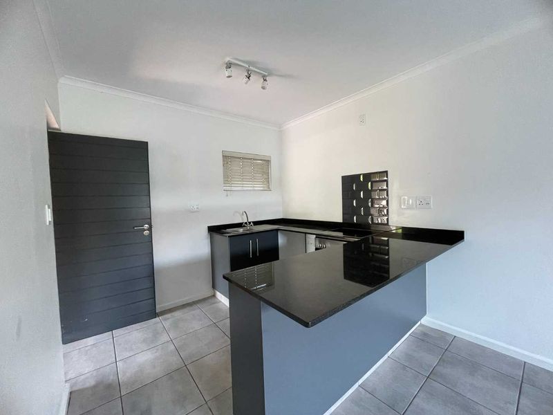 Modern kitchen featuring dark cabinetry, granite countertops, a breakfast bar, and tiled flooring in a clean, open-plan layout.