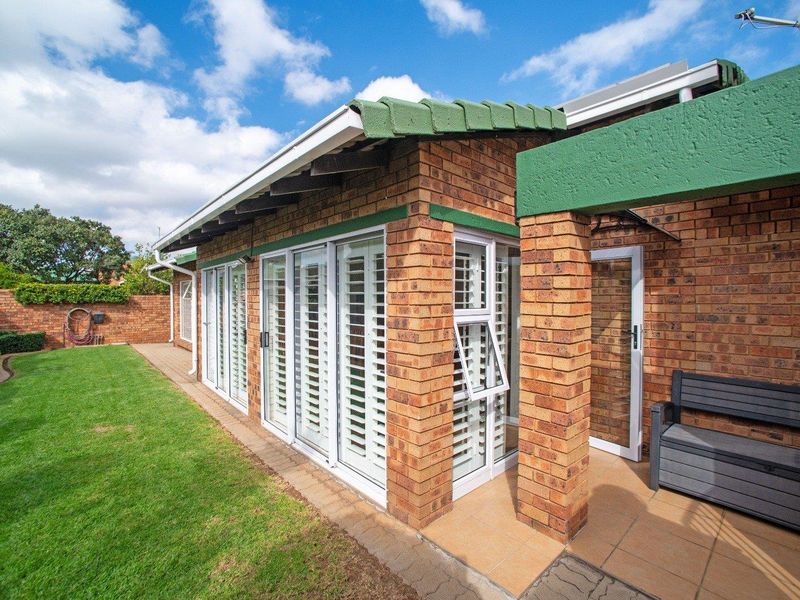 Rear view of the property featuring a face-brick facade, tiled patio area, and white plantation shutters overlooking a well-maintained garden.