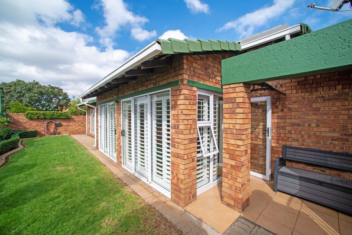 Rear view of the property featuring a face-brick facade, tiled patio area, and white plantation shutters overlooking a well-maintained garden.