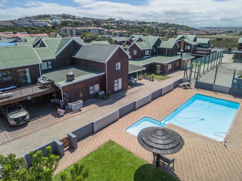 Aerial view of a residential apartment complex featuring a communal swimming pool, paved courtyard, and tennis court facilities.