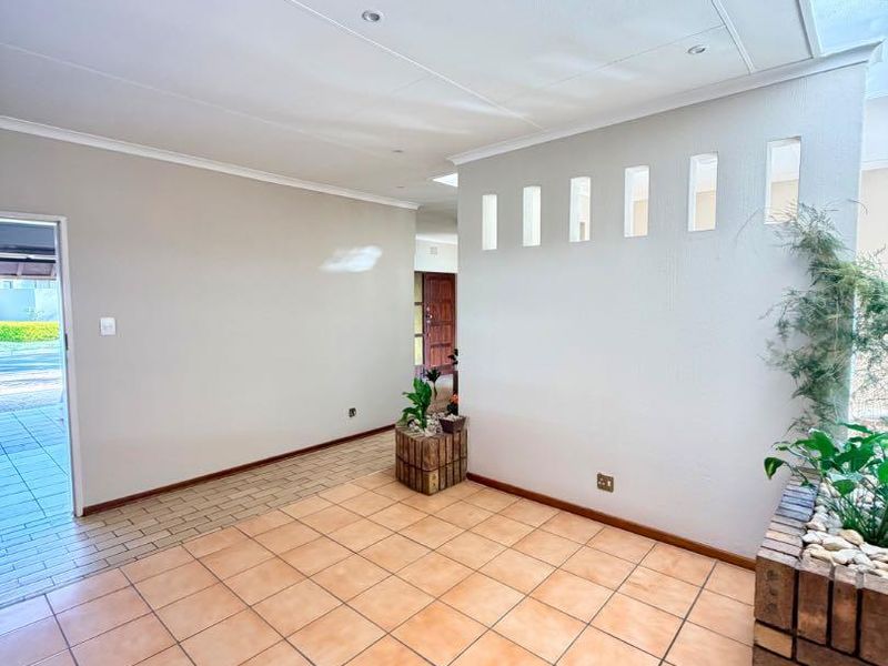 A spacious, light-filled entrance hall featuring ceramic floor tiles, a built-in brick planter, and decorative wall cutouts leading to the main living areas.