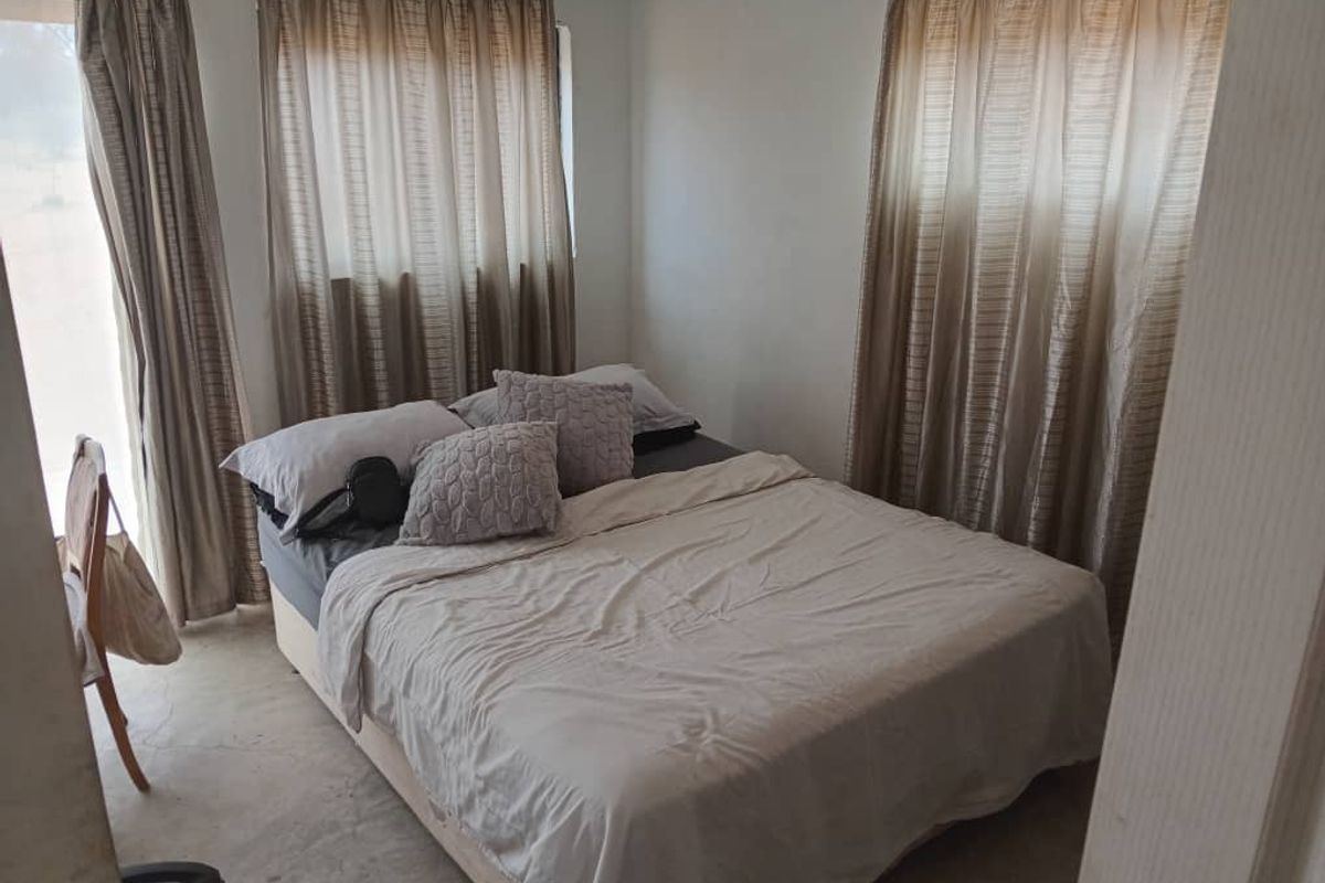 A functional bedroom featuring neutral walls, dual windows with curtains, and exposed concrete flooring.