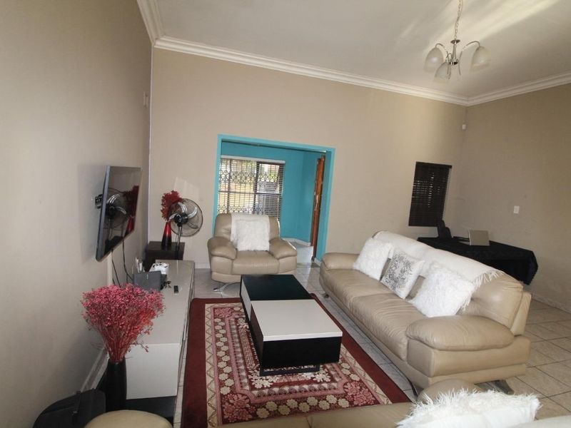 A spacious living room featuring tiled flooring, cove cornicing, and a neutral wall palette, providing a comfortable and functional area for relaxation.