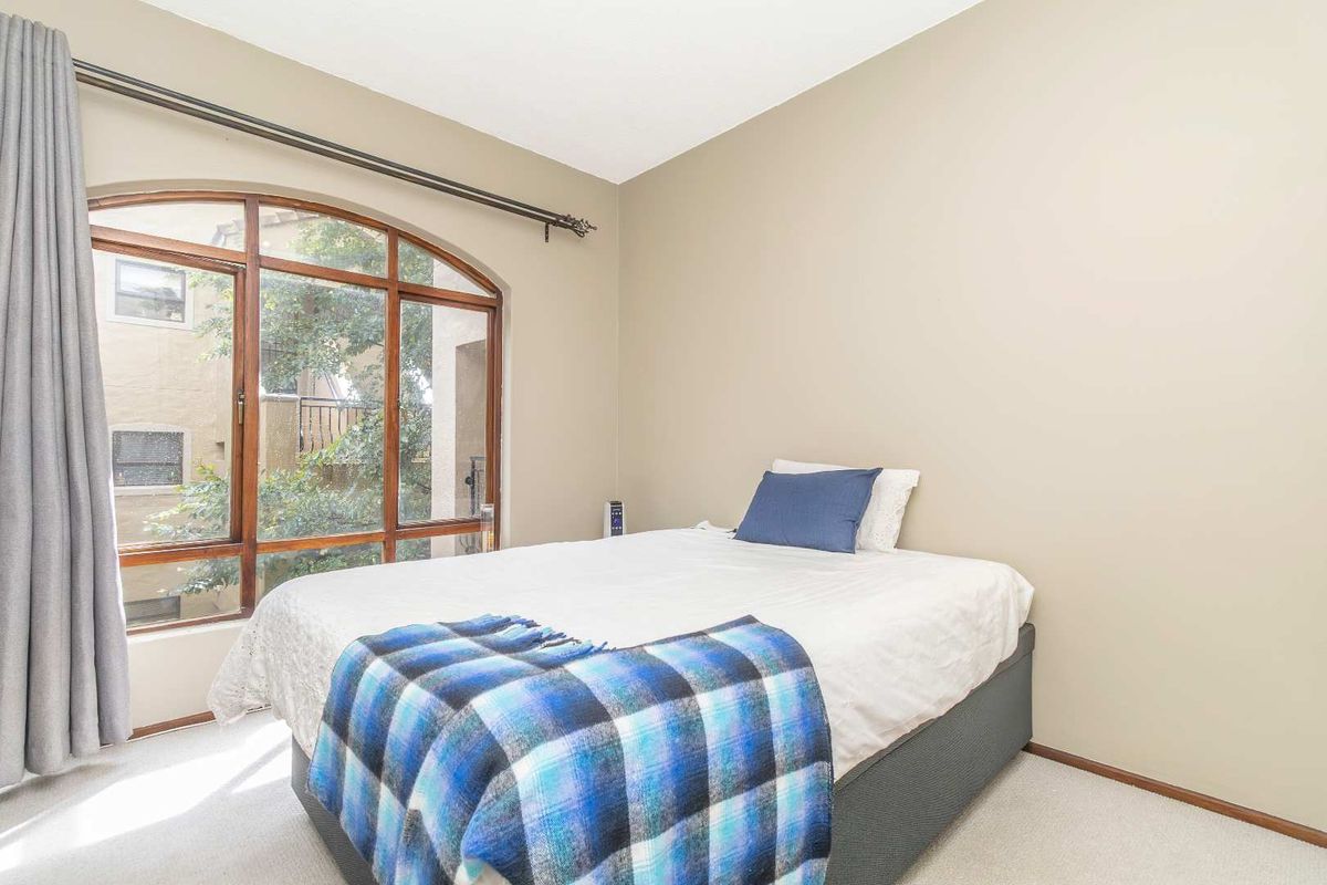 A well-lit bedroom featuring a large arched wooden-framed window, neutral wall tones, and fitted carpeting.