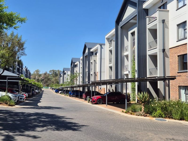 Exterior view of a modern apartment complex featuring paved driveways, covered parking bays, and multi-story residential buildings with balconies.