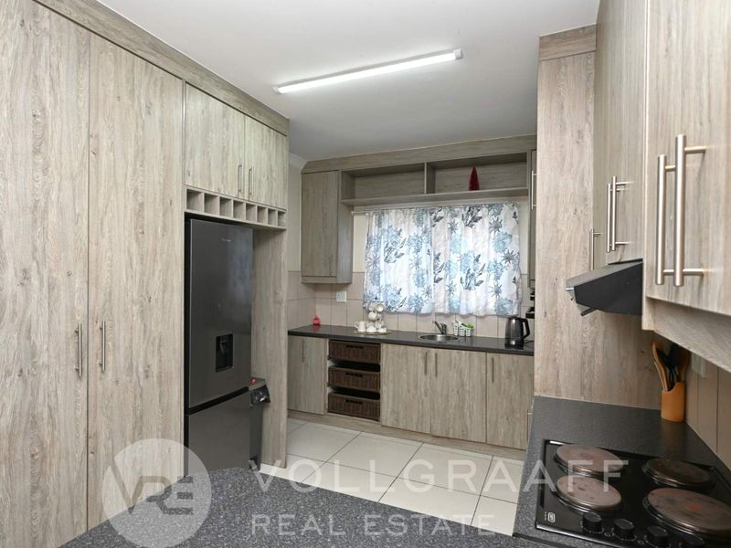 A functional kitchen featuring wood-look laminate cabinetry, dark stone countertops, an electric hob, and an integrated extractor fan.