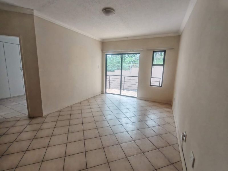 An empty, neutrally painted living room featuring tiled flooring, a coved ceiling, and a sliding glass door providing access to an outdoor balcony area.