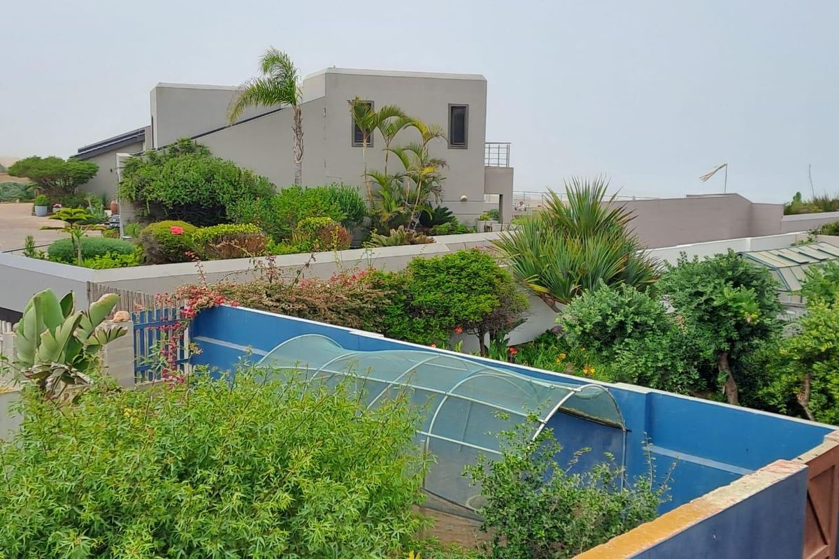 A view of the property's rear garden area featuring established landscaping, a blue boundary wall, and a greenhouse structure.