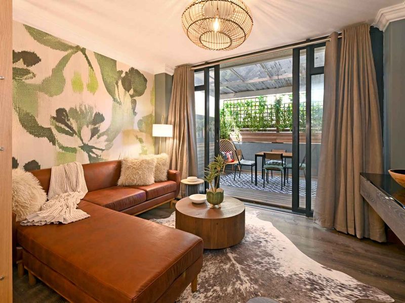 A well-appointed living room featuring modern laminate flooring, crown molding, and large sliding glass doors that provide seamless access to an outdoor balcony area.