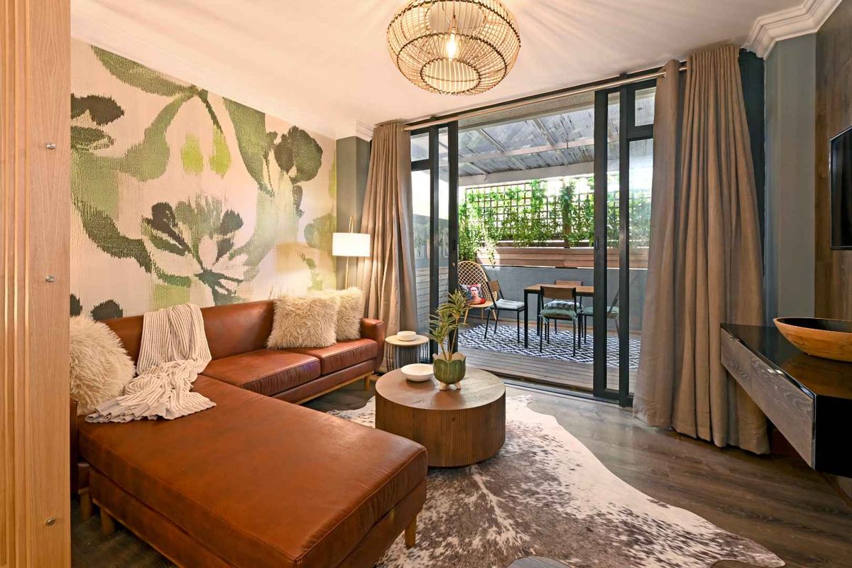 A well-appointed living room featuring modern laminate flooring, crown molding, and large sliding glass doors that provide seamless access to an outdoor balcony area.