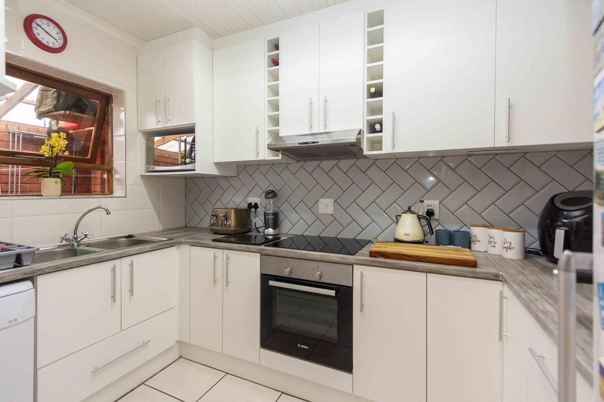 Modern kitchen featuring white cabinetry, herringbone tile backsplash, integrated oven and hob, and durable laminate countertops.