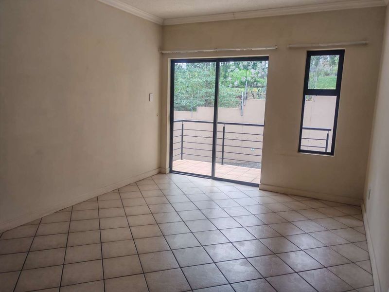An empty living room featuring tiled flooring, neutral walls, and a sliding glass door providing direct access to an outdoor balcony area.