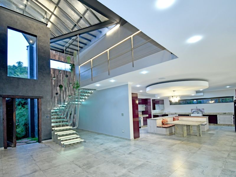 Spacious open-plan living area featuring a striking floating staircase, double-volume ceilings, modern kitchen with stone island, and high-end contemporary finishes throughout.