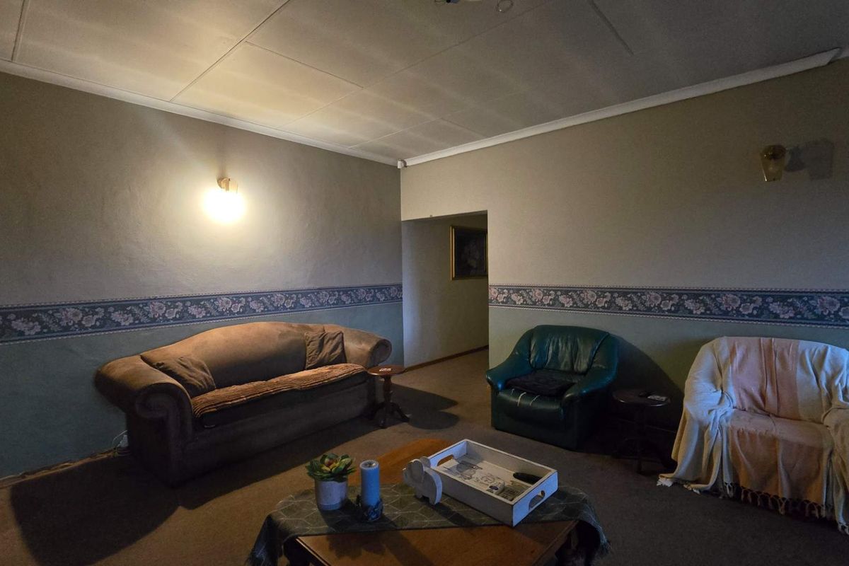 A living room featuring dated wallpaper borders, wall sconces, and a coved ceiling, offering potential for modernization through cosmetic updates.