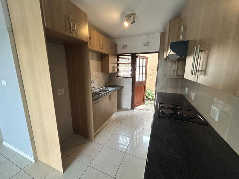 Functional kitchen featuring light wood cabinetry, dark laminate countertops, integrated hob with extractor, and direct access to an outdoor area.