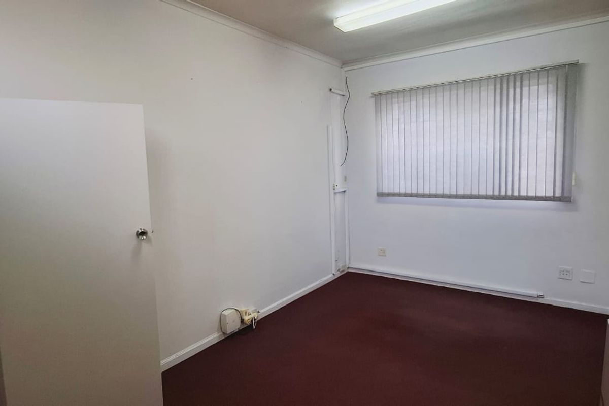 An empty office space featuring carpet flooring, vertical blinds, and a wall-mounted air conditioning unit, suitable for a professional workspace.