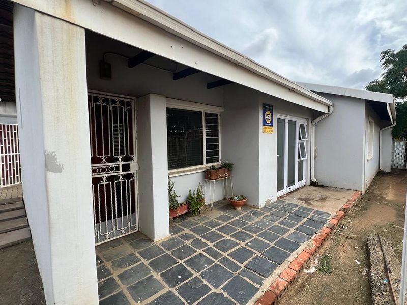 A covered patio area featuring slate tile flooring, security gate access, and sliding glass doors, requiring some exterior maintenance and cosmetic updates.