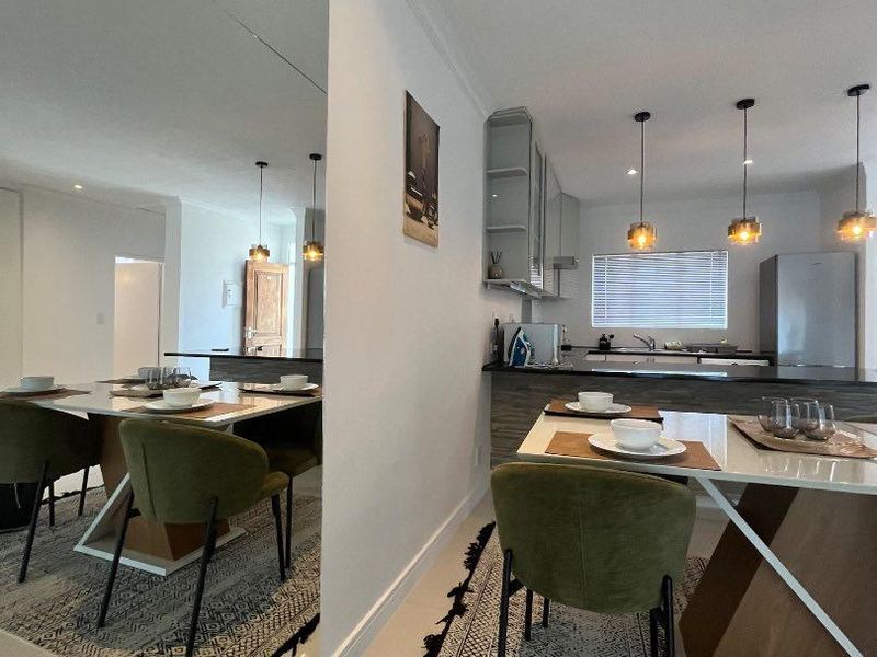 Modern open-plan living and dining area featuring a sleek kitchen with island, pendant lighting, and a large feature mirror reflecting the space.