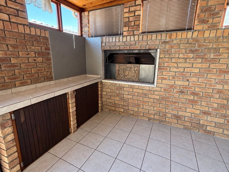Covered patio area featuring a built-in braai, tiled workspace with storage cabinetry, and durable facebrick finishes, ideal for outdoor entertaining.