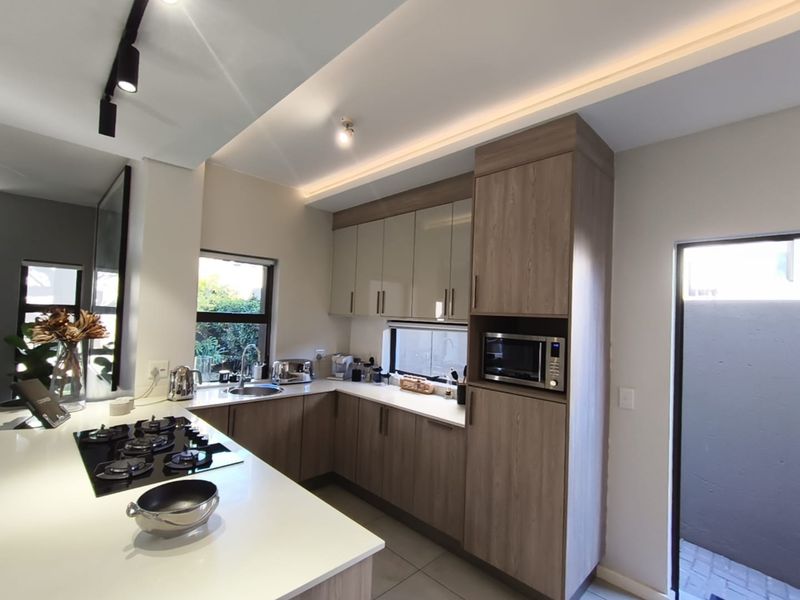 Modern kitchen featuring sleek wood-finish cabinetry, stone countertops, a gas hob, and integrated appliances with recessed ceiling lighting.