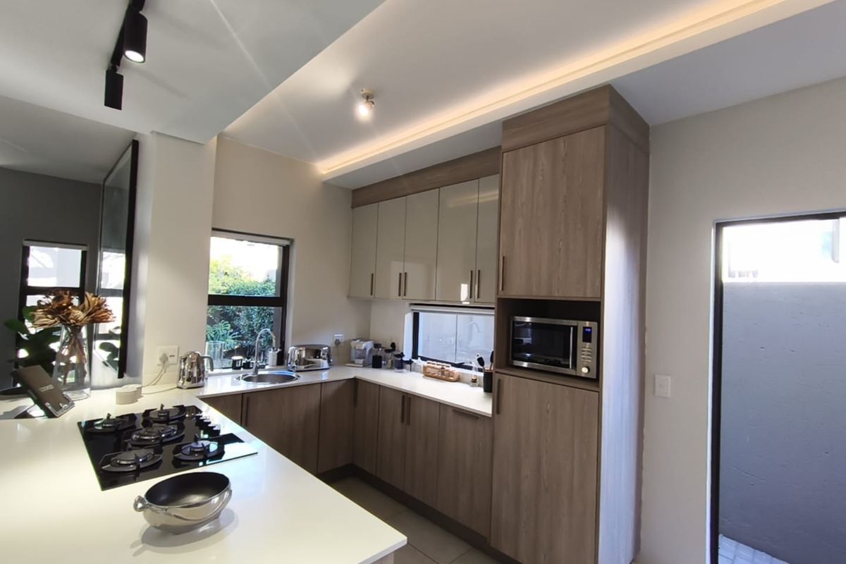 Modern kitchen featuring sleek wood-finish cabinetry, stone countertops, a gas hob, and integrated appliances with recessed ceiling lighting.