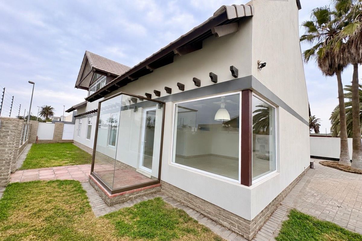 Rear view of the property featuring a glass-enclosed patio, paved pathways, manicured lawn, and secure perimeter electric fencing.