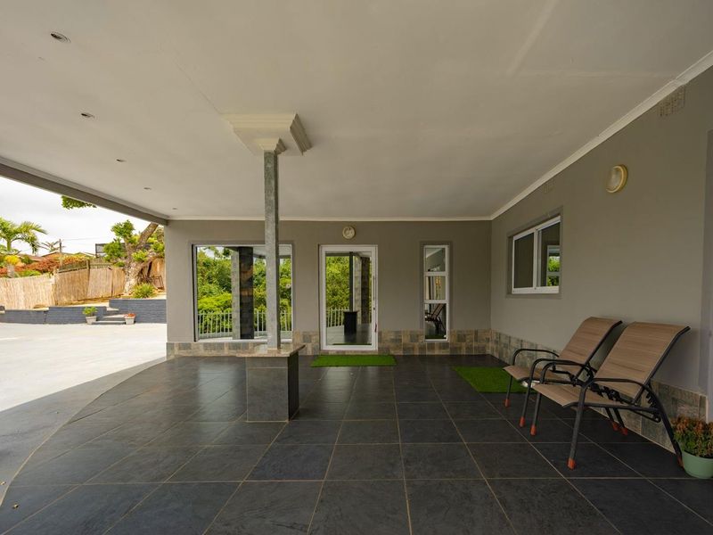 A spacious covered patio featuring dark tiled flooring, recessed lighting, and a structural support column, providing a clean outdoor entertainment area.