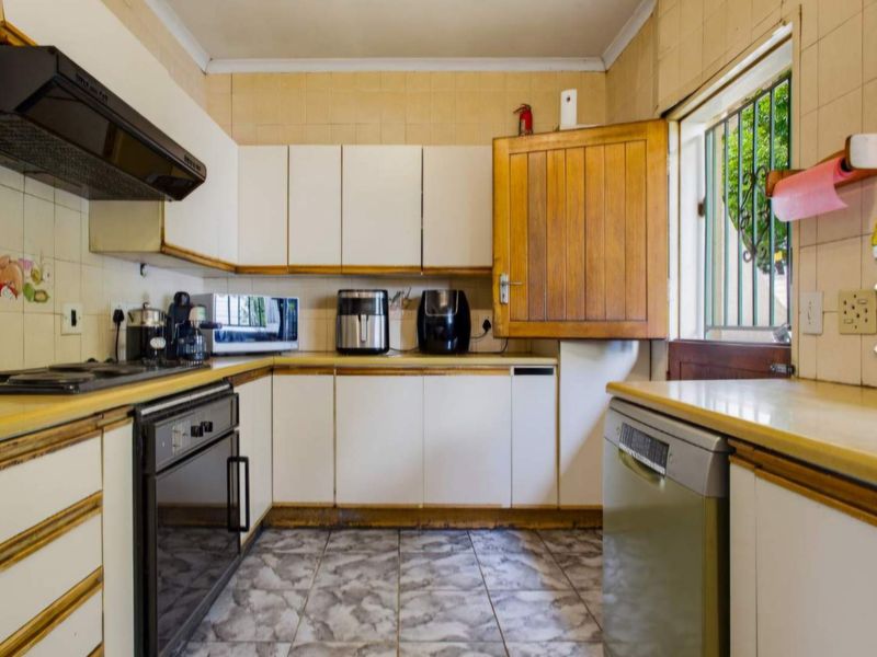 A functional kitchen featuring built-in cabinetry, laminate countertops, a built-in oven, and tiled finishes, offering a dated aesthetic ready for modernization.
