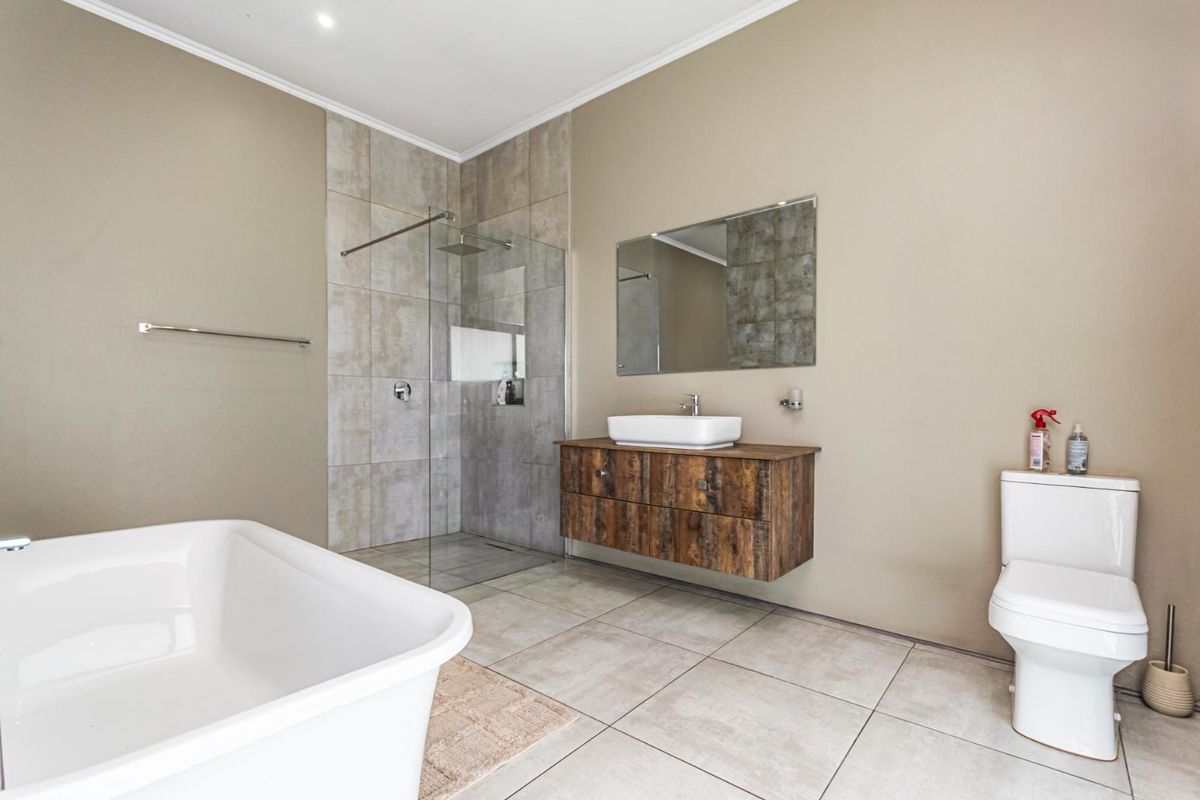Modern bathroom featuring a floating wood-finish vanity, vessel sink, glass-enclosed walk-in shower, and a freestanding bathtub with neutral floor and wall tiling.