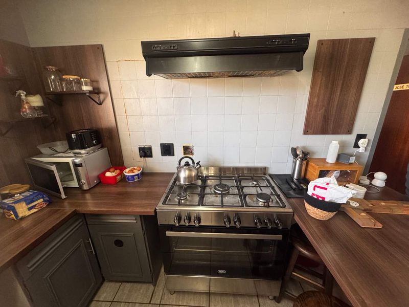 A functional kitchen area featuring a stainless steel gas stove, extractor fan, tiled backsplash, and laminate countertops with built-in cabinetry.