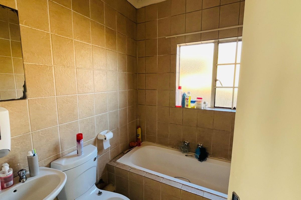 A compact bathroom featuring a built-in bathtub, wall-mounted basin, and toilet, finished with dated floor-to-ceiling ceramic wall tiles.