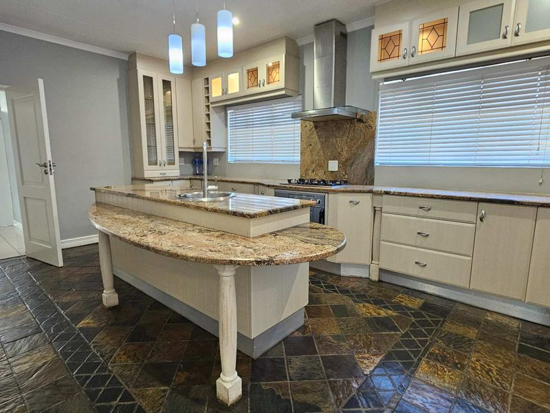 Spacious kitchen featuring granite countertops, a central island with a sink, built-in oven and hob, and durable slate tile flooring.