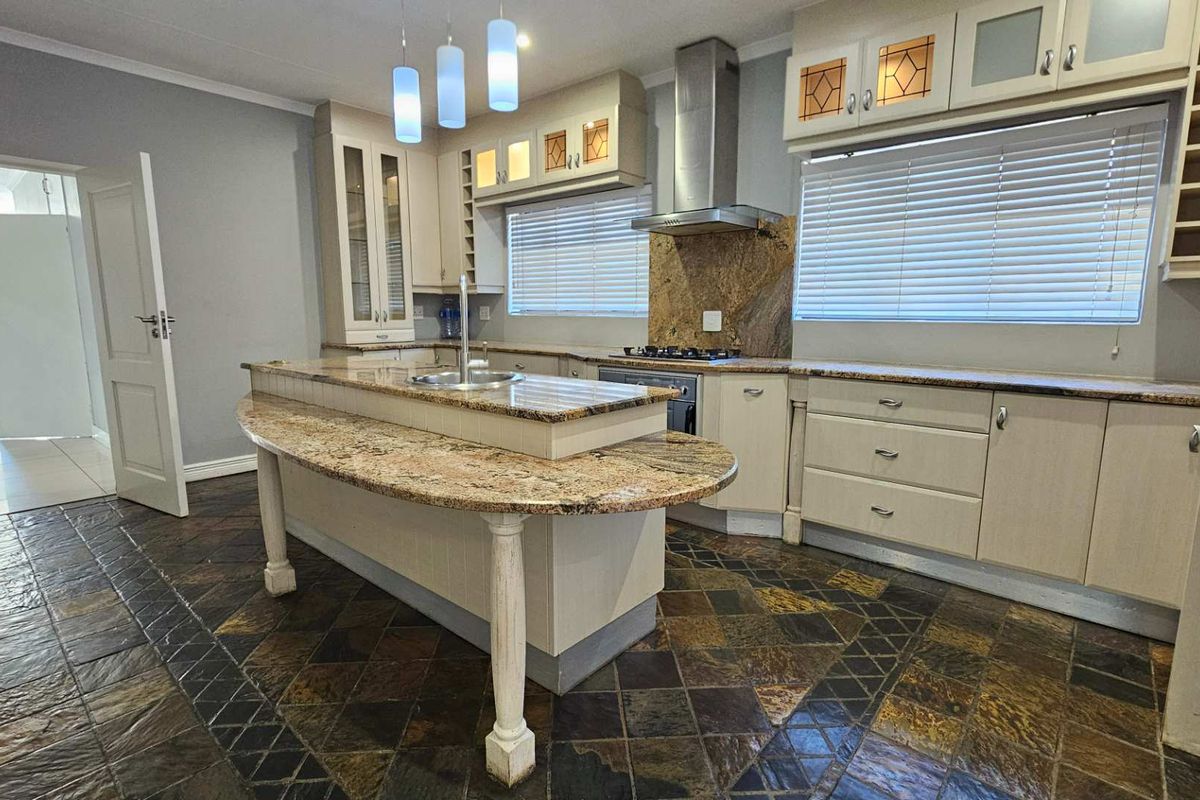 Spacious kitchen featuring granite countertops, a central island with a sink, built-in oven and hob, and durable slate tile flooring.
