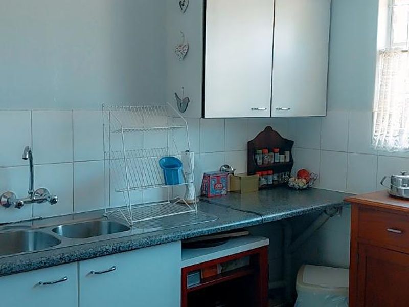 A functional kitchen featuring white cabinetry, laminate countertops, a double sink with mixer tap, and tiled backsplash and flooring.