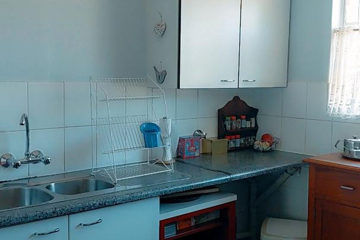 A functional kitchen featuring white cabinetry, laminate countertops, a double sink with mixer tap, and tiled backsplash and flooring.