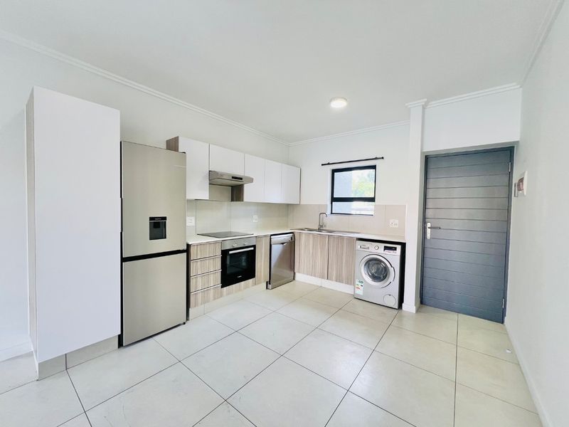 Modern kitchen featuring built-in cabinetry, integrated oven and hob, stainless steel sink, and dedicated plumbing for a washing machine with neutral tiled flooring.