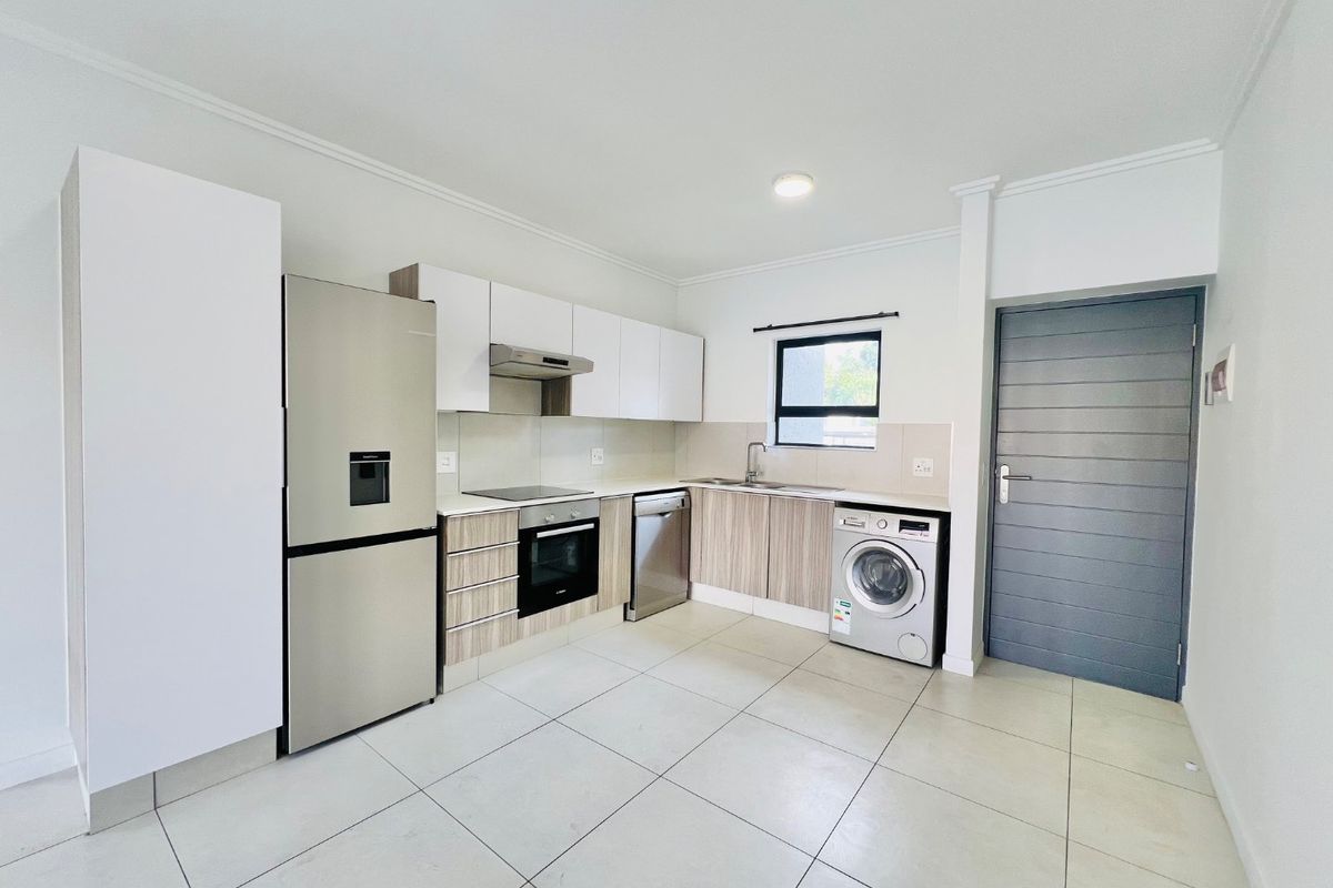 Modern kitchen featuring built-in cabinetry, integrated oven and hob, stainless steel sink, and dedicated plumbing for a washing machine with neutral tiled flooring.