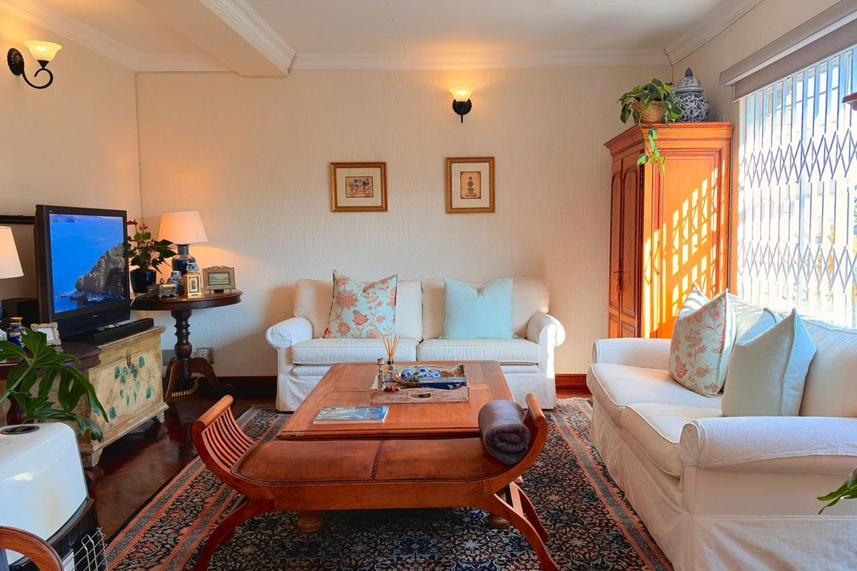 A cozy living room featuring warm wall lighting, crown molding, and large windows with security gates, creating a comfortable and inviting atmosphere.