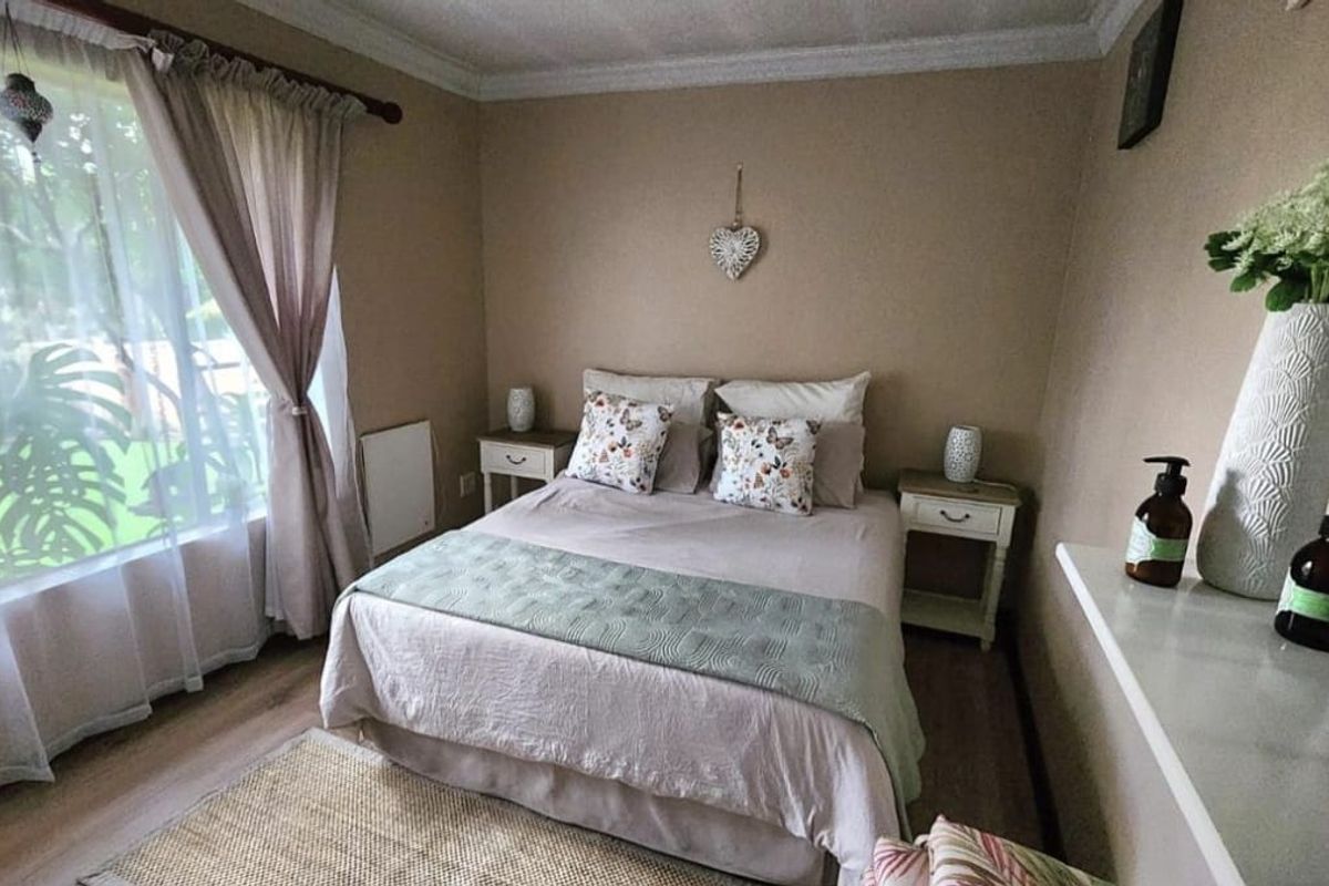 A cozy bedroom featuring neutral wall tones, crown molding, and large windows that provide natural light and garden views.