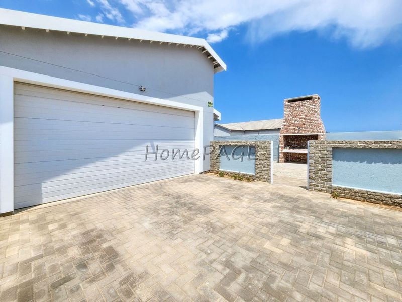 Rear exterior area featuring a paved driveway, automated garage, and a built-in brick braai with stone-clad boundary walls.