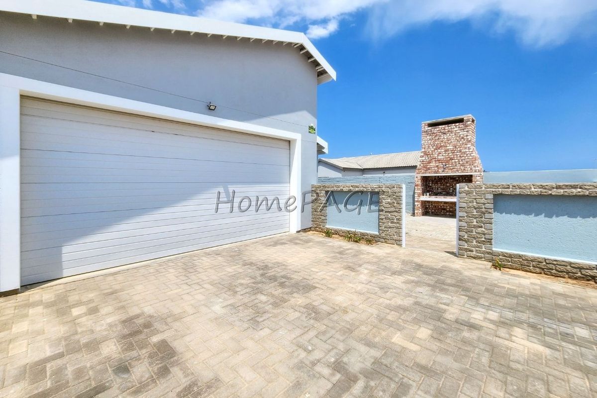 Rear exterior area featuring a paved driveway, automated garage, and a built-in brick braai with stone-clad boundary walls.