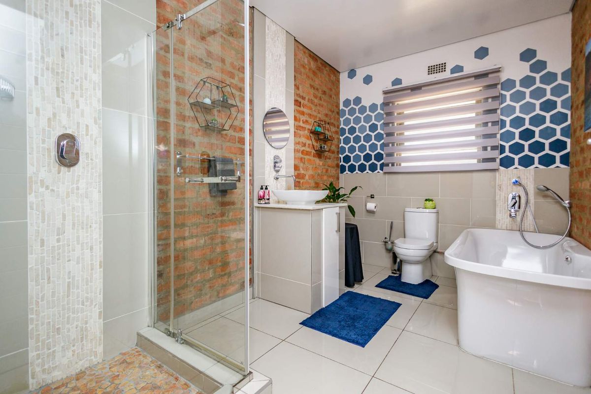 Modern bathroom featuring a glass-enclosed shower, freestanding bathtub, vessel sink vanity, and decorative brick-accented walls with contemporary tiling.