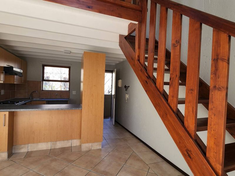Open plan kitchen and living area featuring tiled floors, wooden staircase, and functional kitchen cabinetry with built-in appliances.
