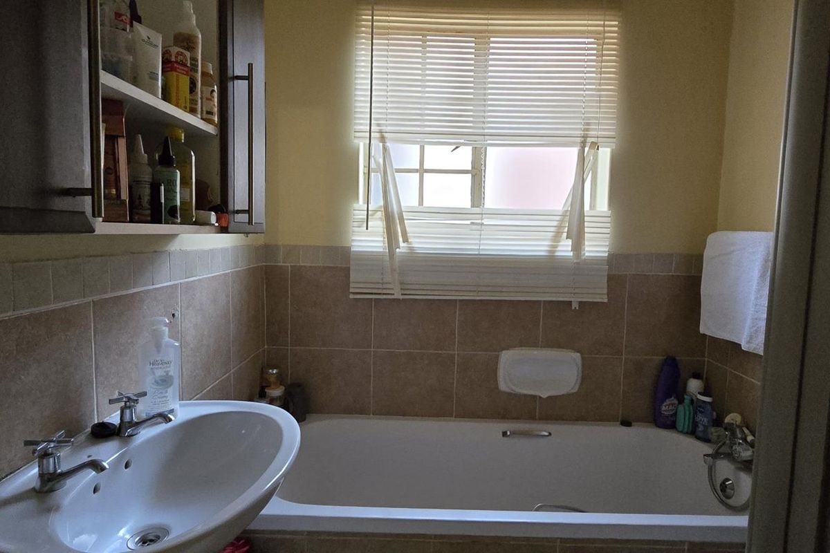 A functional bathroom featuring a built-in bathtub, wall-mounted basin, and tiled splashbacks with overhead cabinetry.