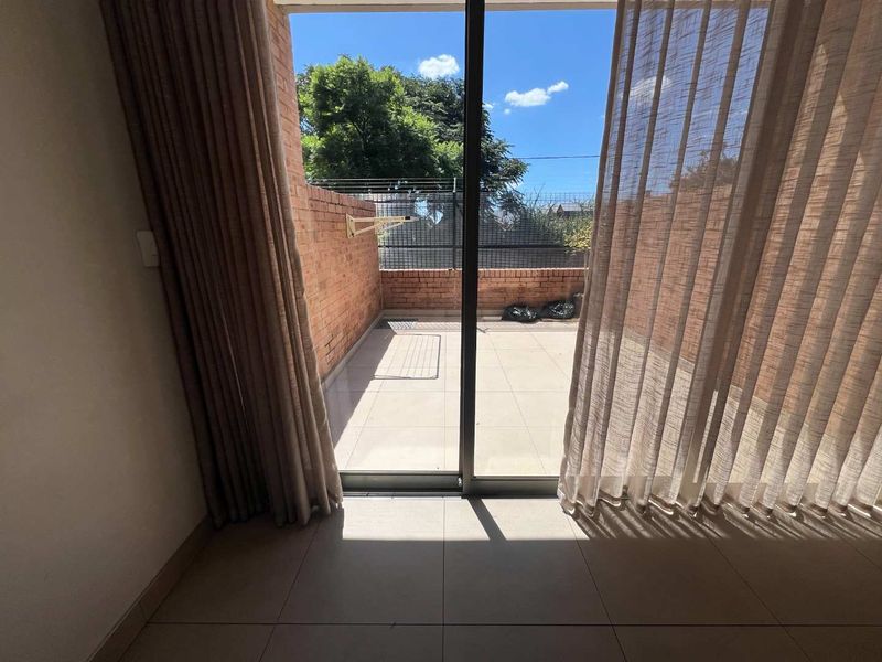 A private outdoor patio area featuring tiled flooring and brick boundary walls, accessible through a large sliding glass door.