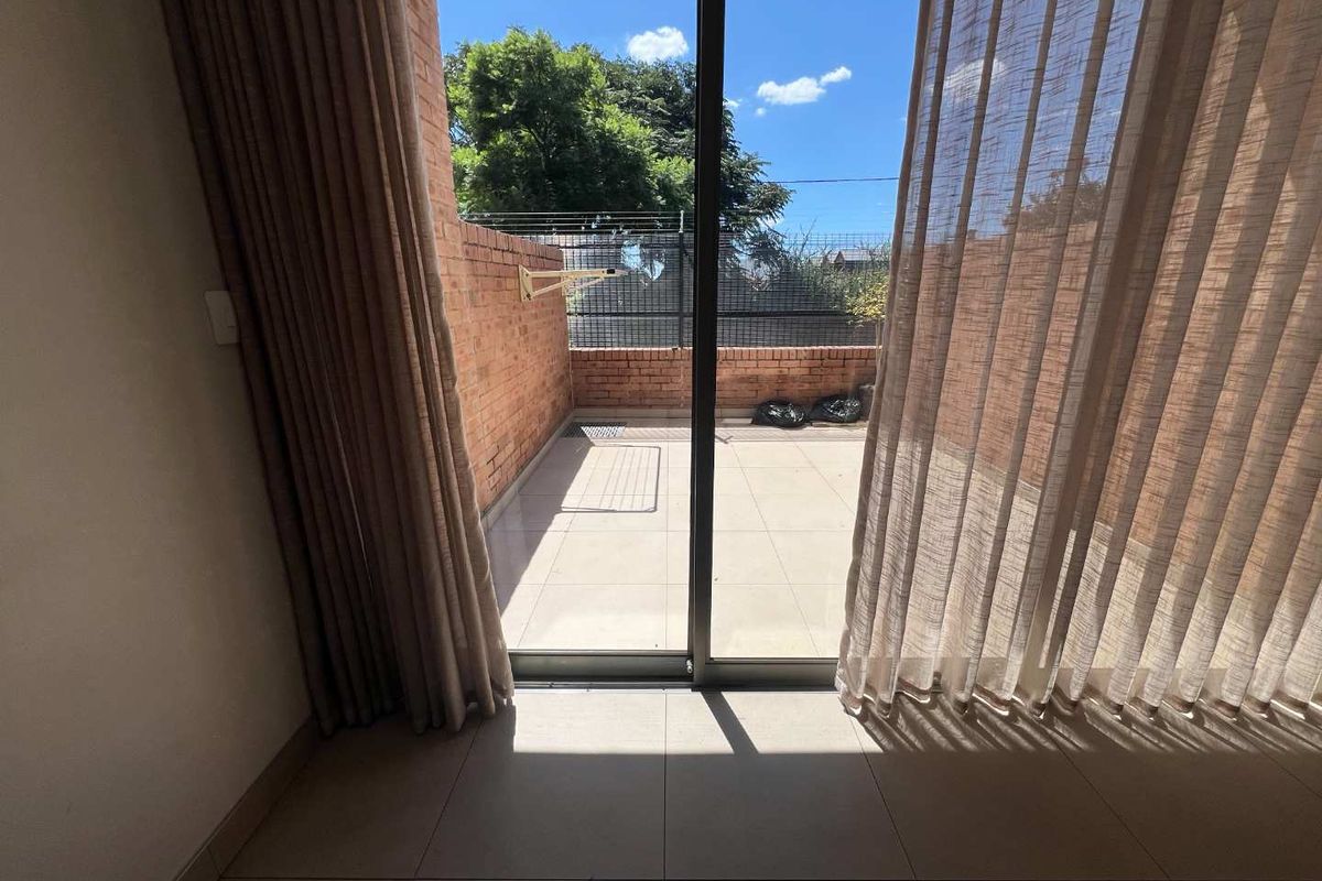 A private outdoor patio area featuring tiled flooring and brick boundary walls, accessible through a large sliding glass door.