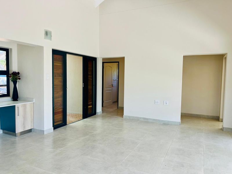 Spacious open-plan living area featuring high vaulted ceilings, neutral tiled flooring, and modern sliding glass doors leading to an outdoor space.