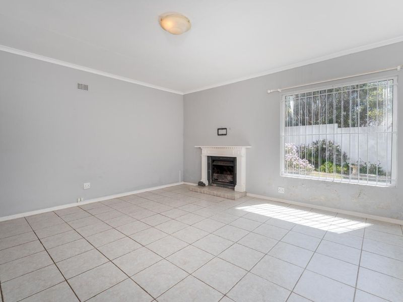 An empty living room featuring tiled flooring, a built-in fireplace, and a large window with security bars, requiring minor cosmetic repairs.